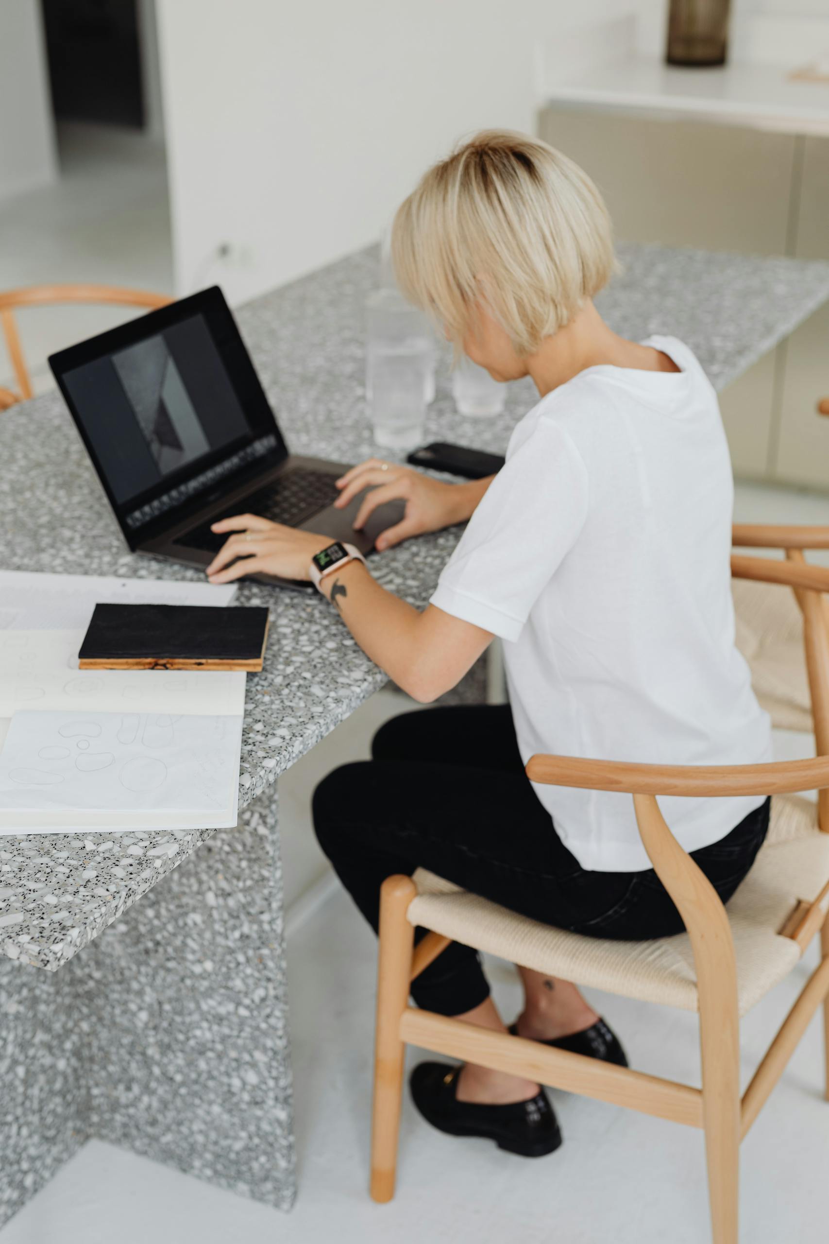 Blonde woman typing on a laptop at a modern granite desk in a minimalist office setting.