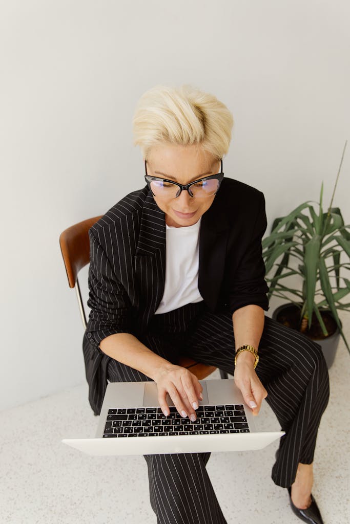 Top view of a businesswoman with short blonde hair working on a laptop in a modern office setting.